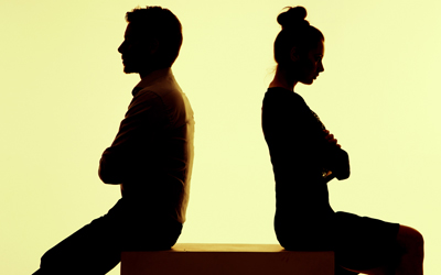 Silhouetted couple against yellow background sitting back to back with arms folded