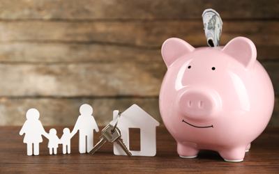 Photograph of a piggy bank, paper cut out of a family of four and a house with a key hanging off the chimney